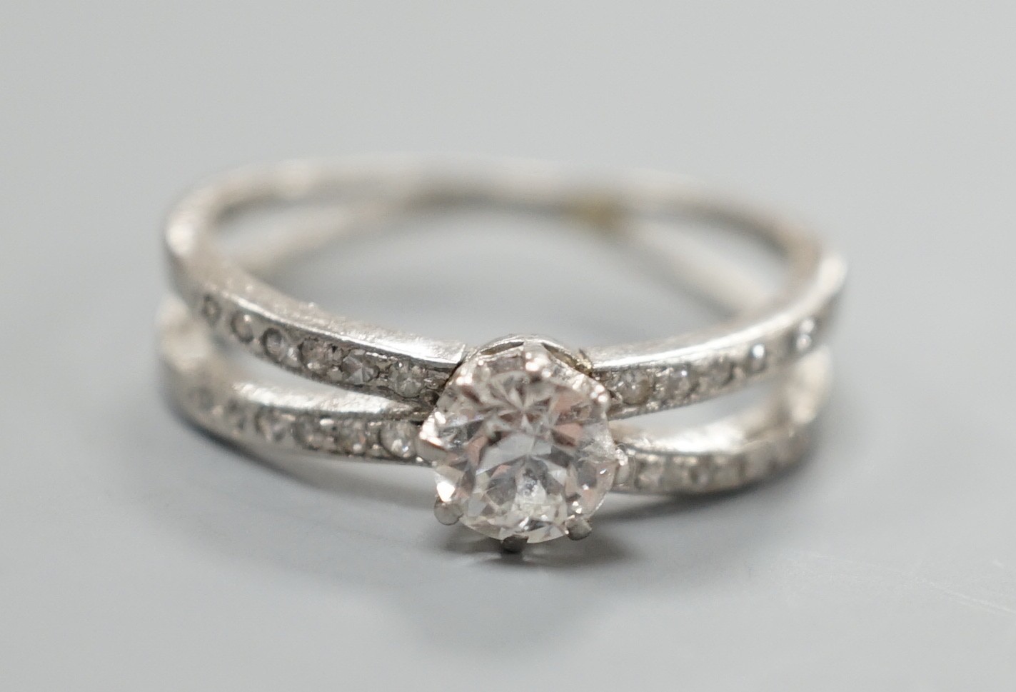 A modern white metal and single stone diamond ring, with diamond chip set crossover shoulders, size K, gross weight 3.3 grams.